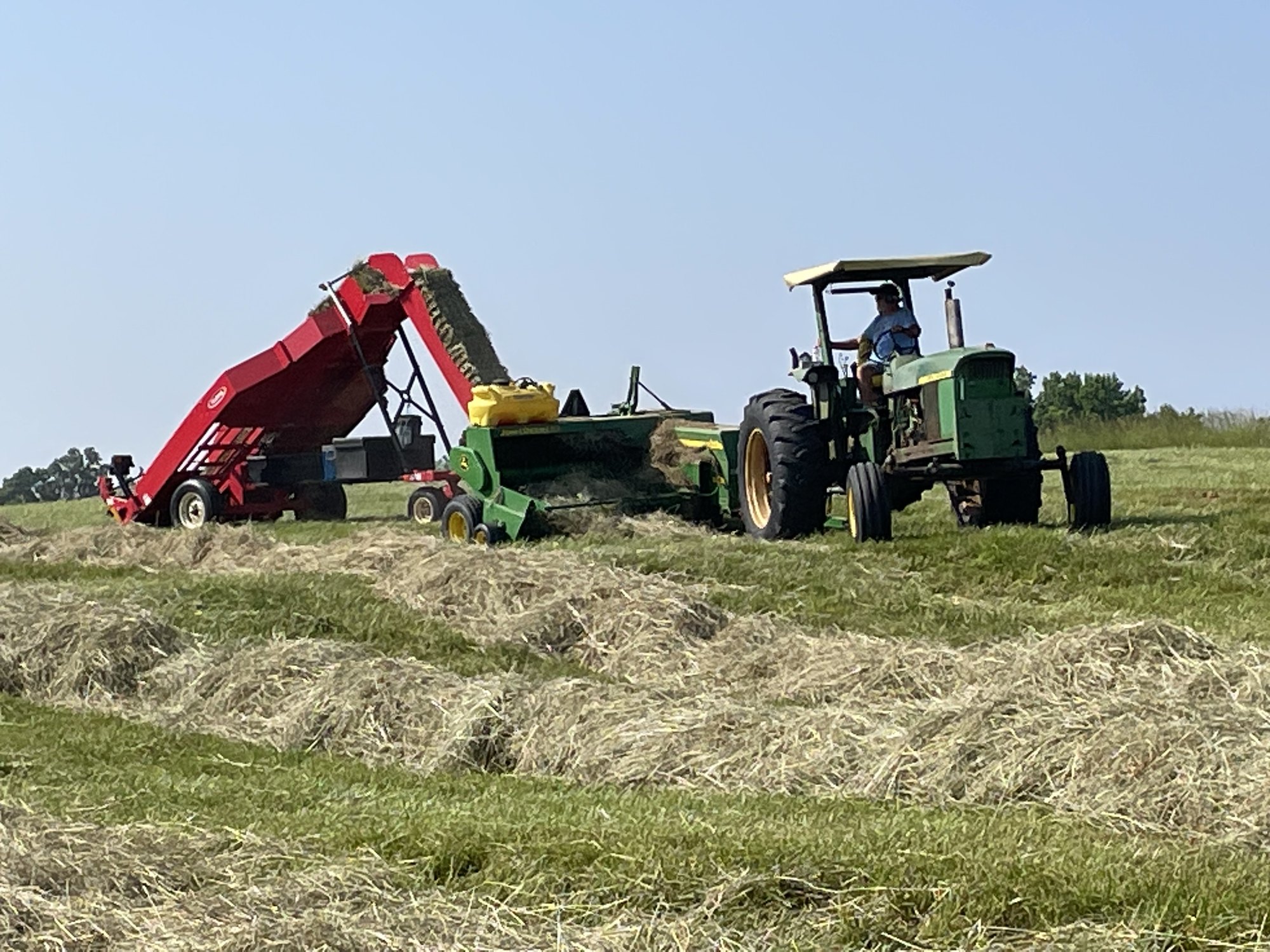 John Deere baler and accumulator working under deep blue summer sky