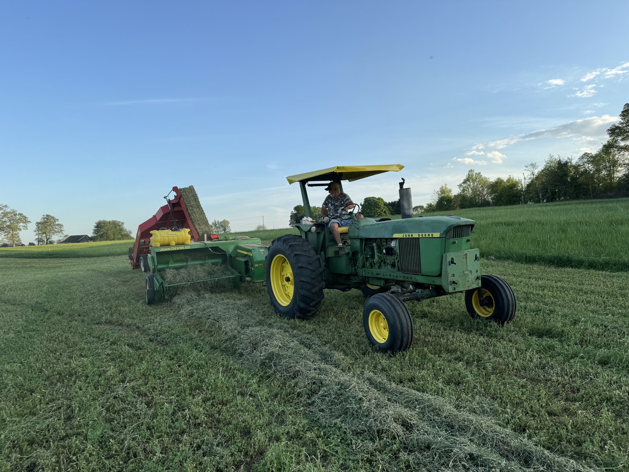 Open-station John Deere baling hay at golden hour